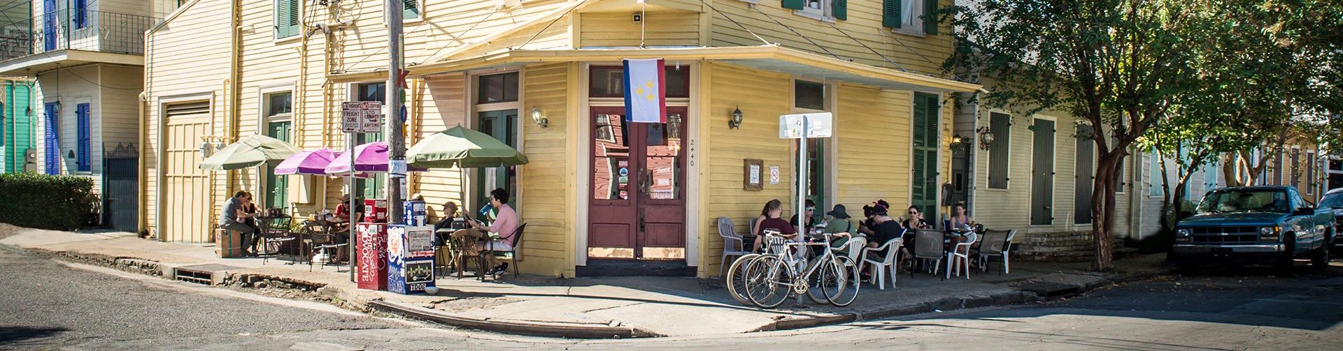 The yellow Cake Café building at the corner of Chartres and Spain in the Marigny, with customers dining at sidewalk tables under umbrellas.